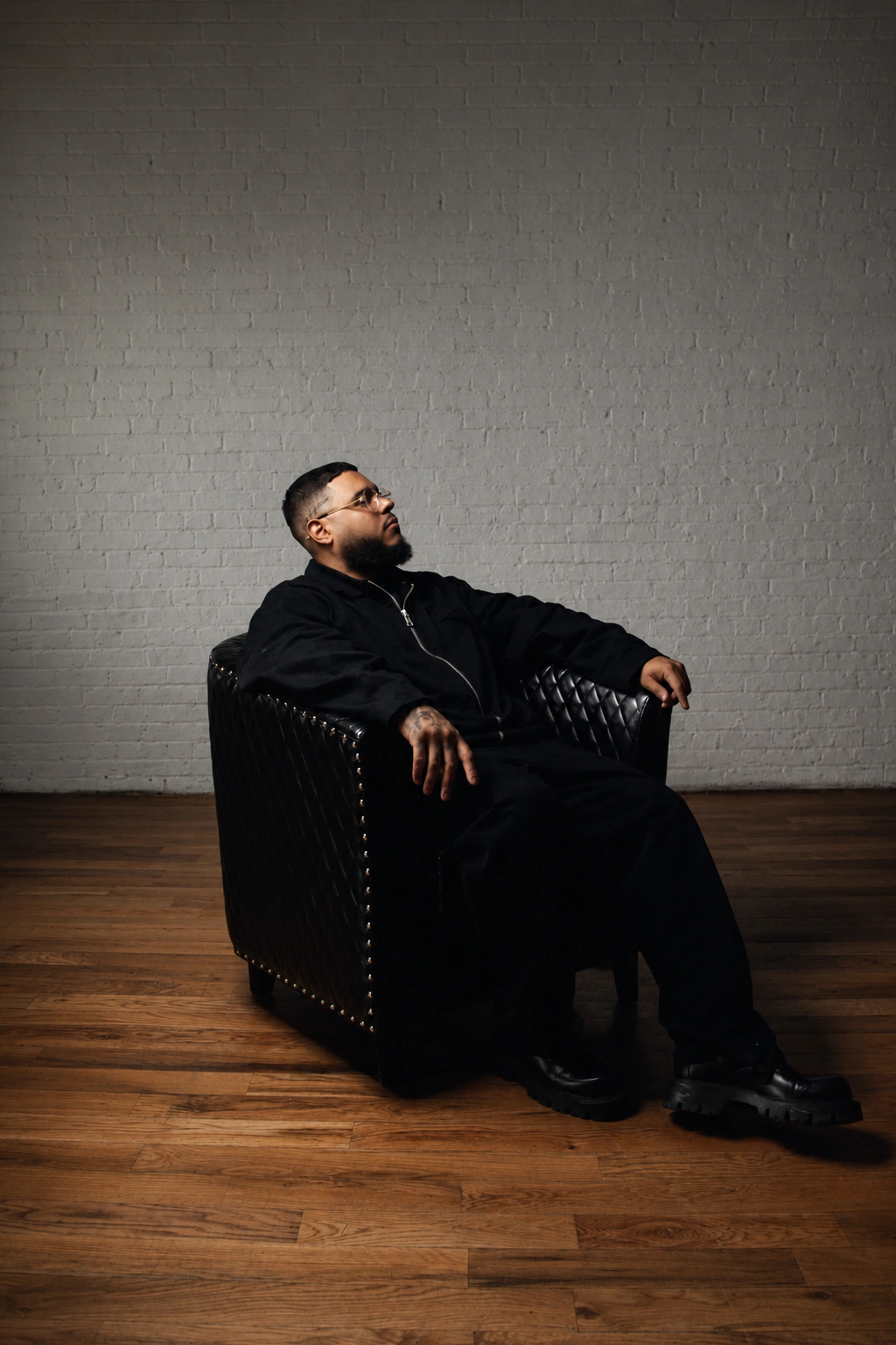 DJ Alaska seated in a black chair against a brick wall